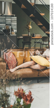 A woman relaxing on the sofa in the living room with her legs stretched out 107014180
