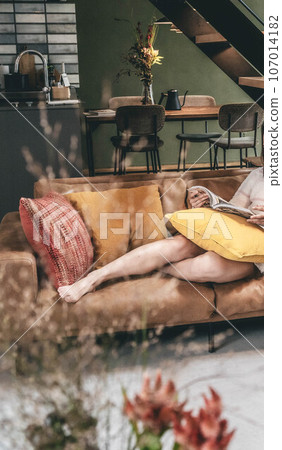 A woman relaxing on the sofa in the living room with her legs stretched out A woman relaxing on the sofa in the living room with her legs stretched out 107014182