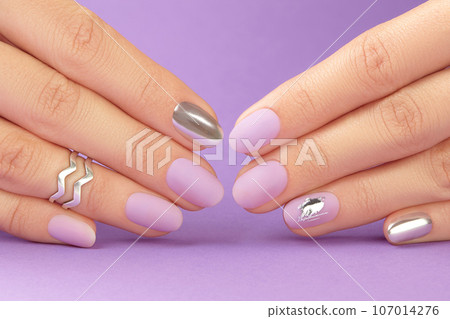 Close up womans hands with matte lavender nail design on purple background 107014276