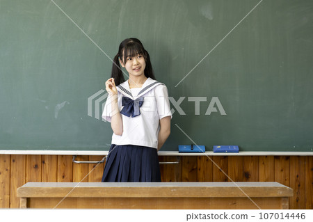 Junior high school girl standing in front of the blackboard with a smile Junior high school girl standing in front of the blackboard with a smile 107014446