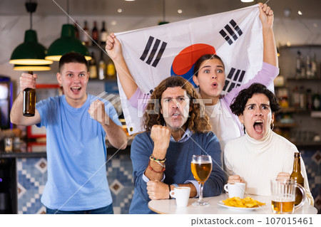 Company of young adult fans supporting team of South Korea with state flag while resting in sports bar with beer 107015461