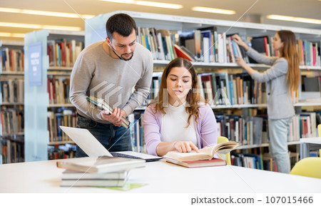 Man working with female colleague on joint project in library 107015466