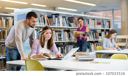 Male librarian helping focused adult student preparing to exam 107015516