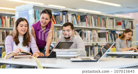 Cheerful students studying in library with books and laptop Cheerful students studying in library with books and laptop 107015645
