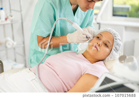 Young male cosmetologist doing cleansing procedure to young woman Young male cosmetologist doing cleansing procedure to young woman 107015688