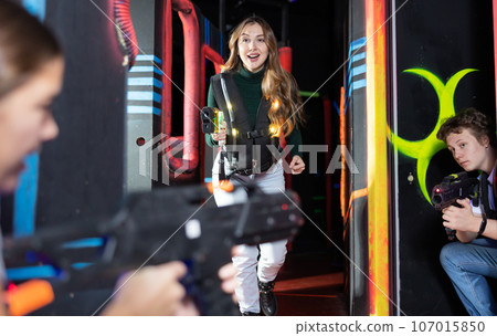 Joyous girl with laser pistol playing laser tag with friends on labyrinth 107015850