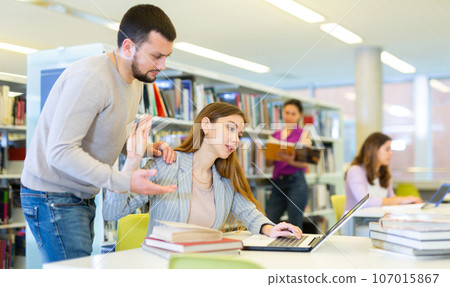 Woman showing stop gesture to annoying man in library Woman showing stop gesture to annoying man in library 107015867