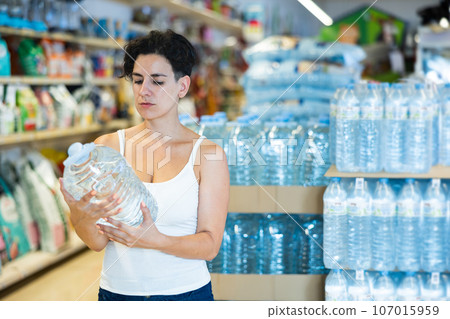Young Hispanic woman reading label on bottle of still water in supermarket 107015959