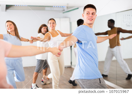 Excited young middle-aged men and women couples turning to sides during pair dance practicing in studio for adults 107015967