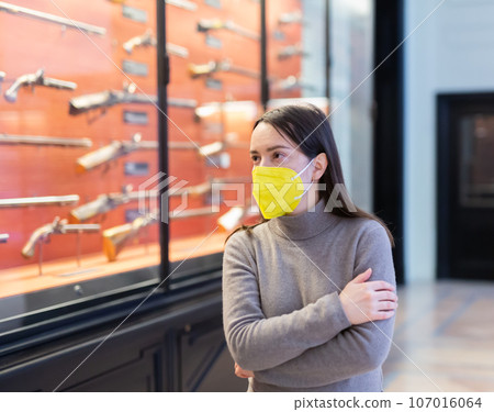 Woman in protective mask examining ancient guns in weapons museum 107016064
