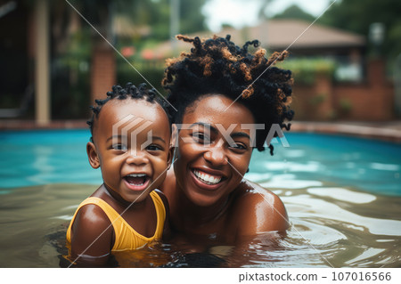 African American mother and her baby are swimming in a pool, smiling, lifestyle family photoshoot 107016566