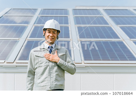 An engineer/business person in work clothes from an electric power company/electrical contractor standing in front of a solar power generation/solar panel 107018664