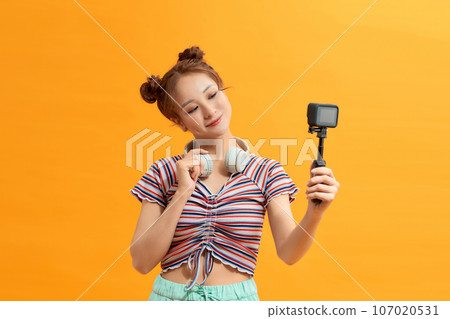 Young woman selfie action cam enjoy over yellow background Young woman selfie action cam enjoy over yellow background 107020531