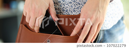 Woman in casual clothes holds her smartphone in her shoulder bag. 107022279