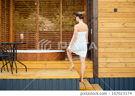 A woman wrapped in towel enters an outdoor jacuzzi 107023174