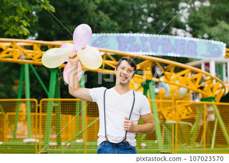 Funny guy is holding a bunch of balloons in his hands at an amusement park waiting for his beloved girl Funny guy is holding a bunch of balloons in his hands at an amusement park waiting for his beloved girl 107023570