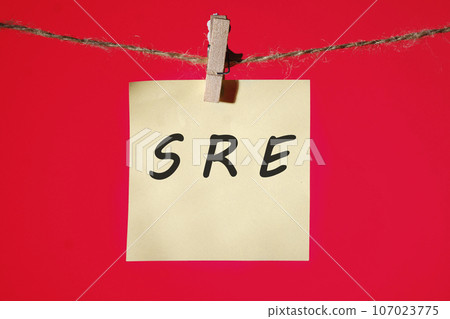 SRE. Site Reliability Engineering text on a yellow sticker hanging on a rope with clothespins on a red background SRE. Site Reliability Engineering text on a yellow sticker hanging on a rope with clothespins on a red background 107023775