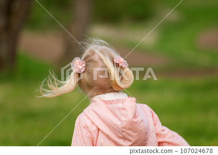 Back view blonde girl with two ponytails in pink outfit running in spring park. Happy girl , spring day 107024678