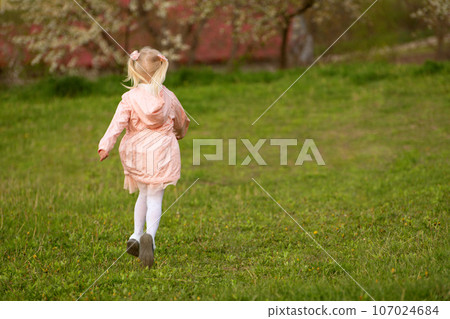 Little European blonde girl with two tails runs through green meadow. Back view. Springtime. Little European blonde girl with two tails runs through green meadow. Back view. Springtime. 107024684