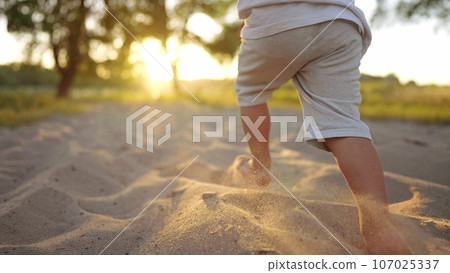 baby run in the park on the sand. bare feet child son run on the sand in the park near the water. happy family kid dream concept. childhood joy baby kid run in the park fun 107025337