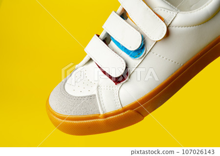 White leather sneakers with fasteners on yellow background White leather sneakers with fasteners on yellow background 107026143