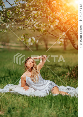 woman garden. she sleeps on a white bed in the fresh spring grass in the garden. Dressed in a blue nightgown. 107027548