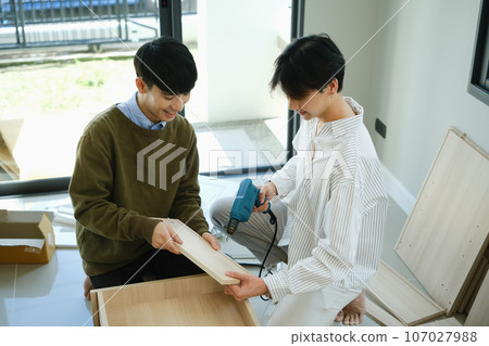 Cheerful gay couple moving in new home and assembles furniture together. LGBTQ, relocation and real estate 107027988