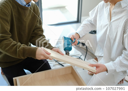 Cropped shot of gay couple talking and using screwdriver for assembling furniture at their new home 107027991