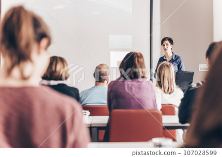 Female speaker giving presentation in lecture hall at university workshop . Participants listening to lecture and making notes. Scientific conference event. Female speaker giving presentation in lecture hall at university workshop . Participants listening to lecture and making notes. Scientific conference event. 107028599