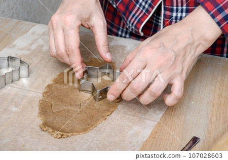 Female hands hold a metal mold for making homemade cookies during preparation for the winter holidays. 107028603