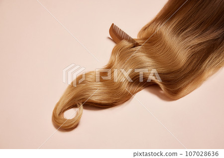 Taking care of long blonde hair with wooden brush on light background. Wavy, healthy, shiny hair look 107028636