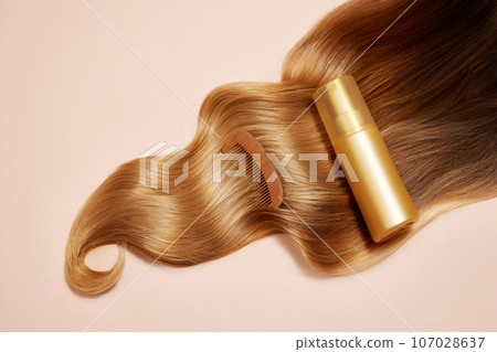 Ply of shiny, wavy, blonde hair with wooden brush and hair product, conditioner, mask over light background. 107028637