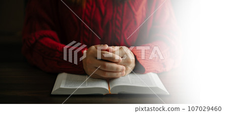 Hands together in prayer to God along with the bible In the Christian concept and religion, woman pray in the Bible on the wooden table. 107029460