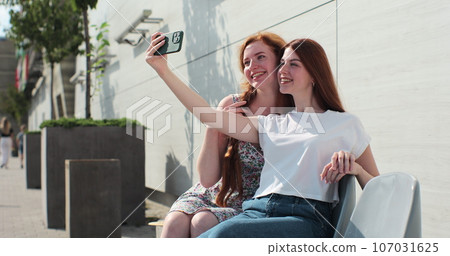 Young lesbian couple taking selfie in the city. Two happy girlfriends pose with rainbow flag. Lgbt woman, showing love to each other. Happy lesbian relationships. Young lesbian couple taking selfie in the city. Two happy girlfriends pose with rainbow flag. Lgbt woman, showing love to each other. Happy lesbian relationships. 107031625