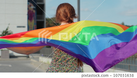 Female is raising up LGBT pride flag, waving it. Lgbt women dancing with pride rainbow flag. 107031638