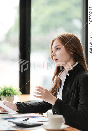 Paperwork. Happy smiling asian business woman sitting at wooden desk in modern office and reading report document. 107032154