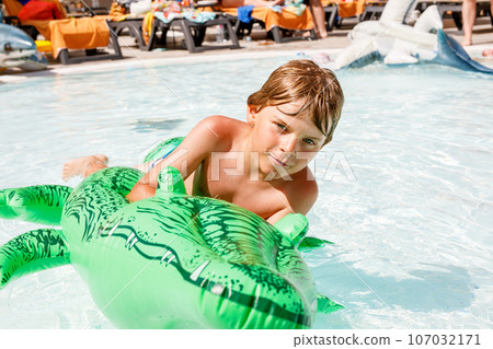 Portrait of happy little kid boy in the pool and having fun on family vacations in a hotel resort. Healthy child playing in water, swimming and splashing. 107032171
