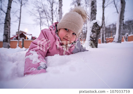 A girl plays in deep snow in the yard. 107033759