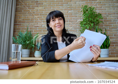 Talking mature businesswoman with documents looking in webcam Talking mature businesswoman with documents looking in webcam 107034524
