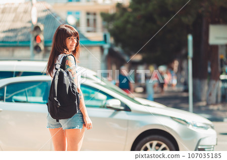 Close up portrait of a woman stands near a road. In the background, a car is driving along the road and traffic light is red. Concept of traffic rules and safety Close up portrait of a woman stands near a road. In the background, a car is driving along the road and traffic light is red. Concept of traffic rules and safety 107035185