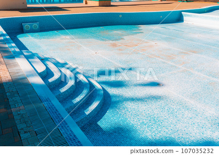 Blue old pool, dry and dirty at the bottom. Copy space. Concept of maintenance and cleaning of swimming pools 107035232