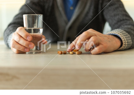 Hands with pills. Senior man hands holding medical pill and glass of water. Mature old senior grandfather taking medication cure pills vitamin. Age prescription medicine healthcare therapy concept Hands with pills. Senior man hands holding medical pill and glass of water. Mature old senior grandfather taking medication cure pills vitamin. Age prescription medicine healthcare therapy concept 107035692