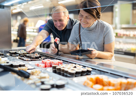 Couple chooses sushi near refrigerator in supermarket 107036520