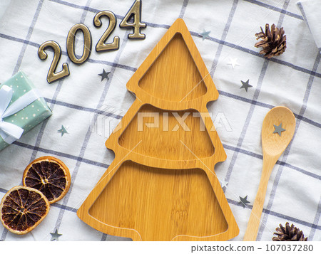 Empty christmas tree shaped wooden plate with 2024 and spoon on towel background Empty christmas tree shaped wooden plate with 2024 and spoon on towel background 107037280