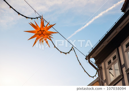 Beautiful Moravian star or Herrnhuter Stern street glowing decoration hanged on wall german city street at christmas advent winter holidays. Traditional Xmas ornament decor in Germany 107038094
