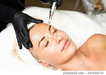 Microneedle RF lifting procedure. A cosmetologist performs a facial rejuvenation procedure on a woman. Hardware cosmetology. 107038274