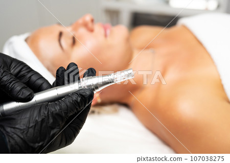 Microneedle RF lifting procedure. A cosmetologist performs a facial rejuvenation procedure on a woman. Hardware cosmetology. Microneedle RF lifting procedure. A cosmetologist performs a facial rejuvenation procedure on a woman. Hardware cosmetology. 107038275