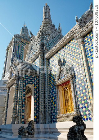 A sunlit temple with intricate spires, adorned with blue, yellow, and white tiles, and a golden door, stands under a clear blue sky. 107039219