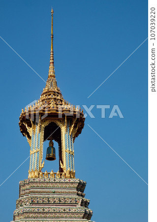 A resplendent Thai temple bell tower, crowned with a gleaming golden roof and adorned with vibrant details, stands proudly against the backdrop of a flawless blue sky. 107039220