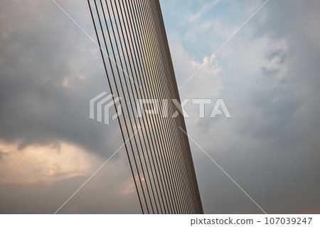 A suspension bridge cable, composed of smaller cables, extends diagonally against a cloudy sky. A suspension bridge cable, composed of smaller cables, extends diagonally against a cloudy sky. 107039247